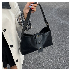Close-up detail of black PU leather shoulder bag with gold metal eyelets and vertical stitching