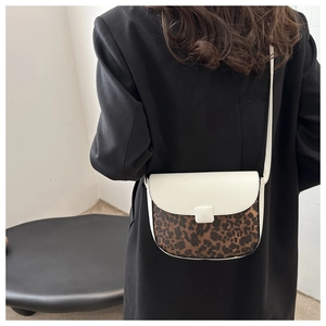 Model view of a leopard print and white leather saddle bag worn with a black coat