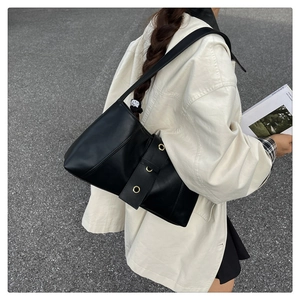 Close-up of black PU leather shoulder bag with golden eyelets on a wide strap