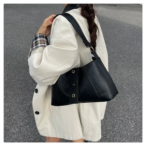 Close-up of a minimalist black underarm bag with gold rivet accents on a stylish model