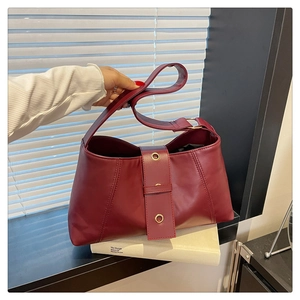 Detail of burgundy leather shoulder bag featuring golden metallic grommets and rich texture
