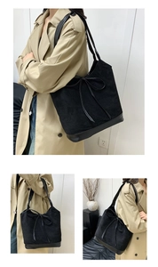 Detail view of large black tote bag with suede texture and leather bow decoration