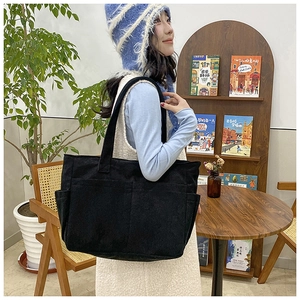 Side view of a large black corduroy tote bag with multiple pockets worn by a model