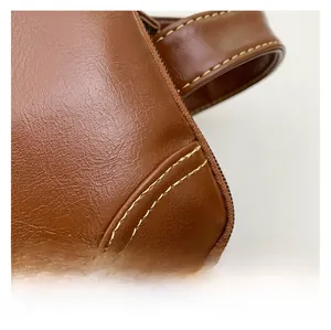 Detail view of brown pebbled leather texture with sturdy stitching on luxury travel bag