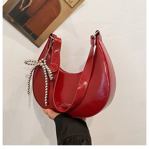 Detail of red crescent bag with glossy cracked texture and silver bead bow charm