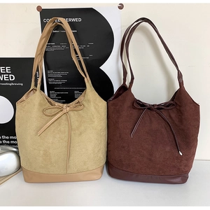 Detail of khaki and brown suede tote bags with decorative bows and shoulder straps
