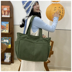 Detail of green corduroy tote bag with dual front pockets in a casual lifestyle setting