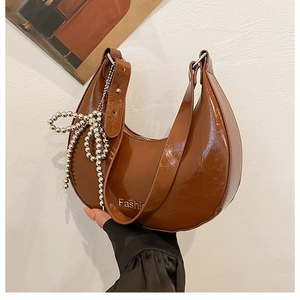 Detail of a brown glossy half-moon bag with a metallic bead bow pendant and zipper