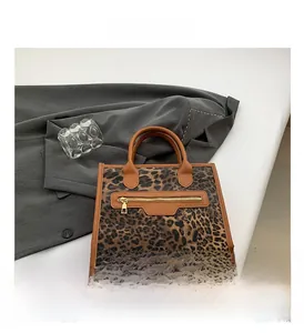 Detailed close-up of leopard print tote bag with brown leather handles and gold metal zipper