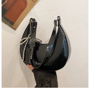 Detail of black cracked lacquer underarm bag with silver beaded bow and Fashion text
