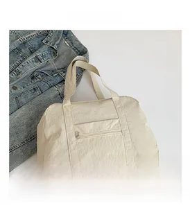 Detail view of large beige nylon travel bag with front zipper pocket and soft texture