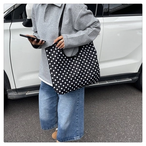 Detail of a large black canvas tote bag with white polka dots on a shoulder carry strap