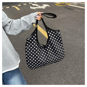 Detail of a large canvas tote bag with white polka dots on black held by a model
