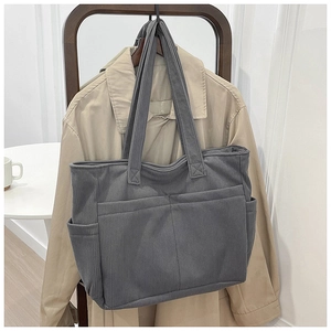 Detailed view of grey corduroy tote bag with multiple pockets hanging on a wooden hanger