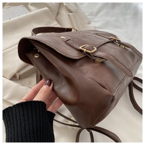 Close-up of brown vintage leather backpack showing metal buckles and embossed letter details