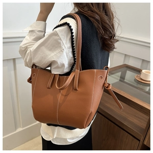 Close-up of caramel brown pebble leather tote bag with white stitching and leather knot detail