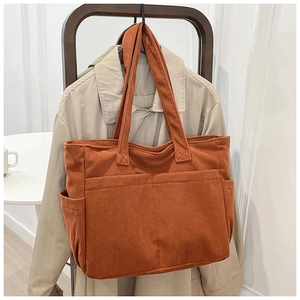 Macro view of textured orange corduroy tote bag featuring functional front storage pockets