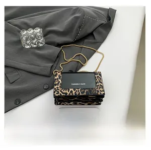 Detail of leopard print bag with golden chain and accordion folds on grey fabric