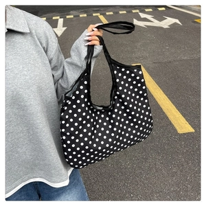 Detail of a large black tote bag with white polka dots featuring long shoulder straps