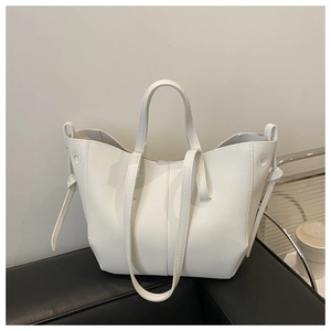 Detail of white lychee pattern tote bag with decorative side ties on black furniture