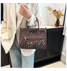 Detail of leopard print tote bag with brown leather handles and golden zipper hardware