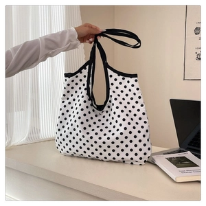 Close-up of black polka dot canvas tote bag with black strap in a minimalist setting