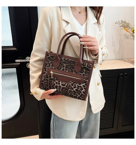 Detail view of leopard print tote bag with brown leather handles and front metal zipper