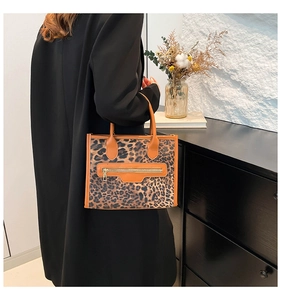 Detailed close-up of a leopard print tote bag with brown leather trim and metal zipper