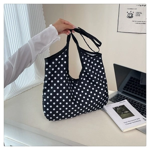 Detail of a large capacity black polka dot canvas tote bag held by hand in a lifestyle setting