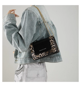 Detail view of leopard print crossbody bag with gold chain and black flap on denim jacket