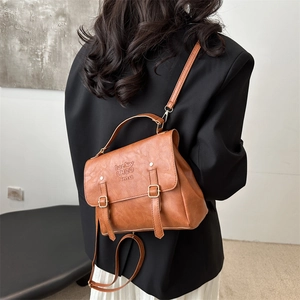 Rear view of model wearing a vintage brown faux leather backpack with embossed text