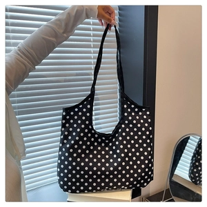 Vertical view of a large black tote bag with white polka dots and long shoulder straps