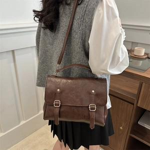 Close-up of vintage dark brown faux leather satchel with buckle straps and textured finish