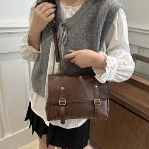 Close-up of vintage dark brown faux leather messenger bag with buckle straps and embossed text