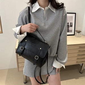 Detailed view of black litchi texture leather messenger bag with gold buckles