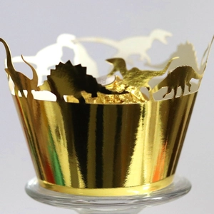 Golden dinosaur laser cut cupcake wrappers for birthdays and parties shown on a glass stand