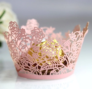 Detail of pink laser-cut floral cupcake wrapper with intricate rose pattern and gold chocolate