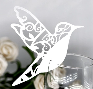 Close-up of laser-cut hummingbird place card with intricate floral patterns on a glass rim