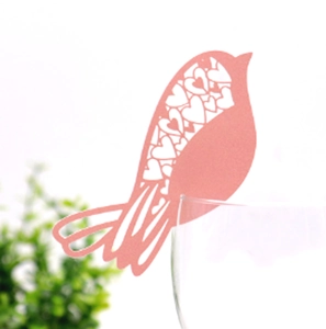 Detail of pink bird place card with heart laser-cut design on a glass rim for weddings