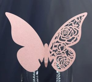 Detailed laser-cut pink glitter butterfly name card with rose pattern on a glass rim