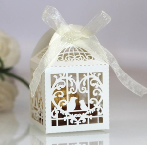 Detail of laser-cut white wedding favor box with bird pattern and white organza ribbon