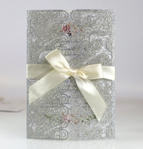Detail of laser-cut wedding invitation with silver glitter lace and white satin bow