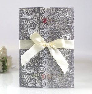 Close-up of glittery silver laser-cut floral wedding invitation with silk bow decoration
