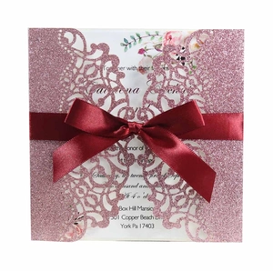 Close-up of laser-cut glitter pink wedding invitation with a deep red satin ribbon bow
