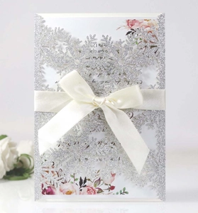 Elegant laser-cut silver glitter snowflake invitation card with a white satin ribbon bow