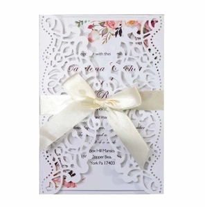 Detail of laser-cut floral wedding invitation with white lace sleeve and satin ribbon bow