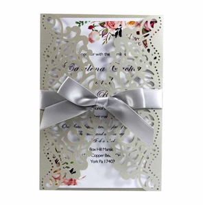 Detail of laser-cut wedding invitation in champagne gold with elegant silver ribbon knot
