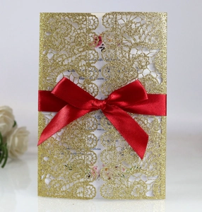 Macro detail of laser cut glitter gold lace wedding invitation with red satin ribbon bow