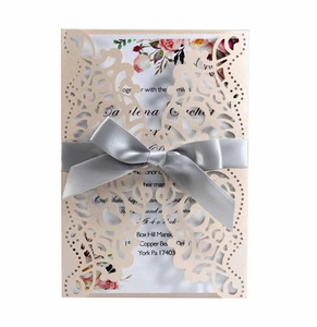 Detailed laser-cut wedding invitation with beige floral sleeve and silver satin bow