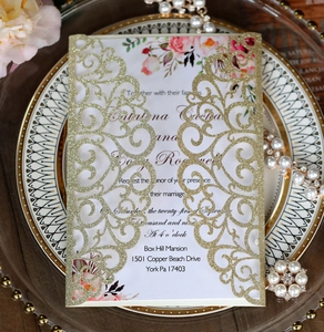 Macro detail of laser-cut wedding invitation with gold glitter texture and floral card